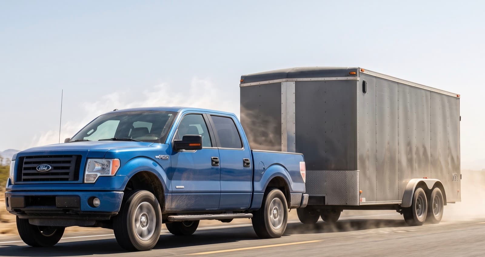 Pickup truck towing an enclosed cargo trailer down a hot, dusty highway